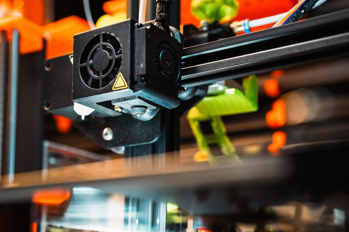 Detalhe de uma impressora 3D depositando filamento com iluminação azul e laranja.