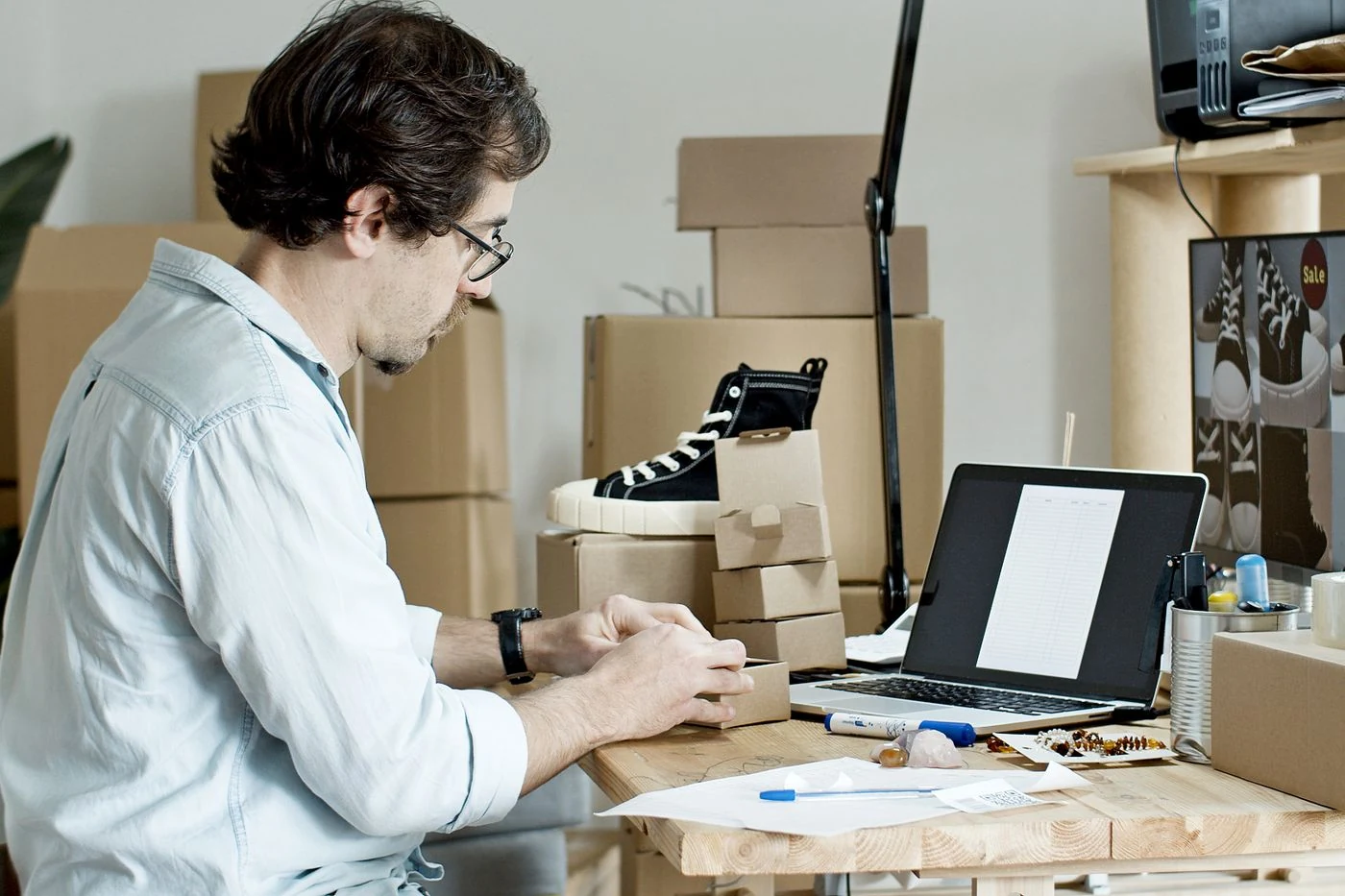 Empreendedor preparando pedidos de uma loja virtual ao lado de um notebook.