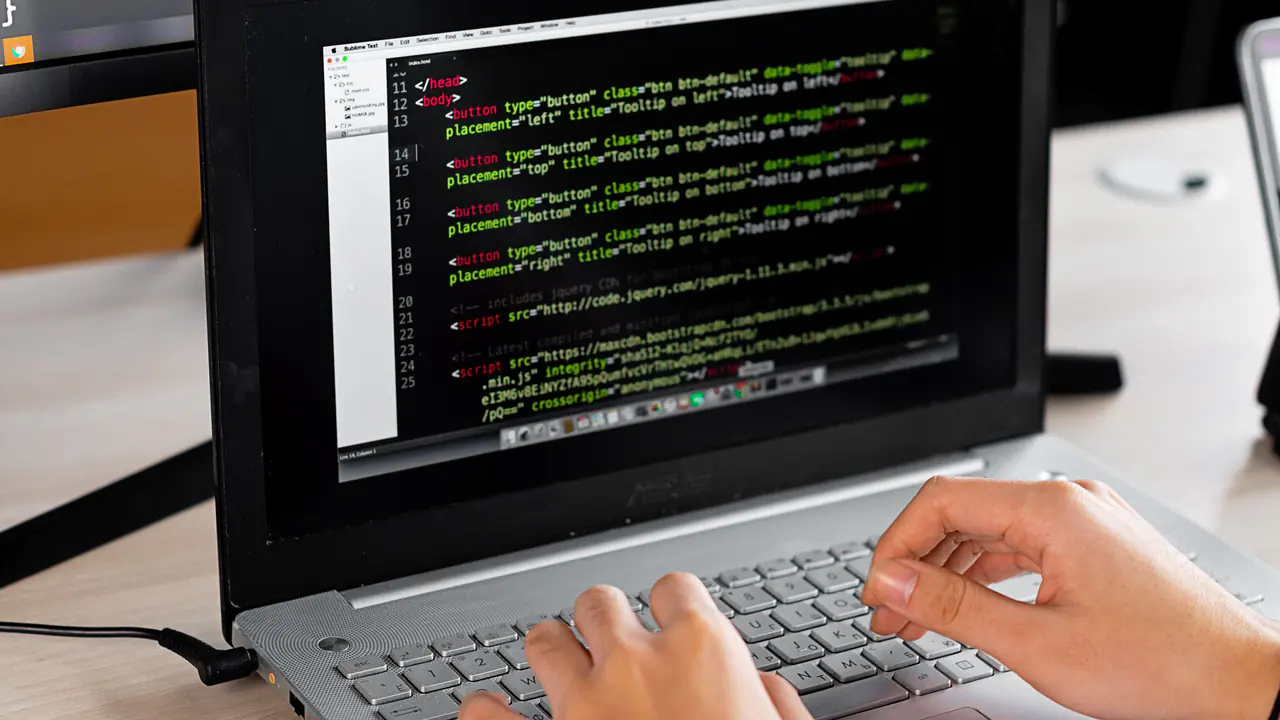 Pessoa programa em uma mesa com notebook e monitor externo.