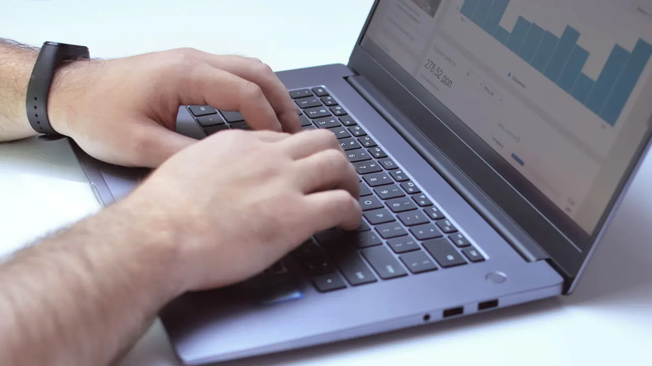 Mãos digitam em notebook com gráficos de análise abertos na tela.