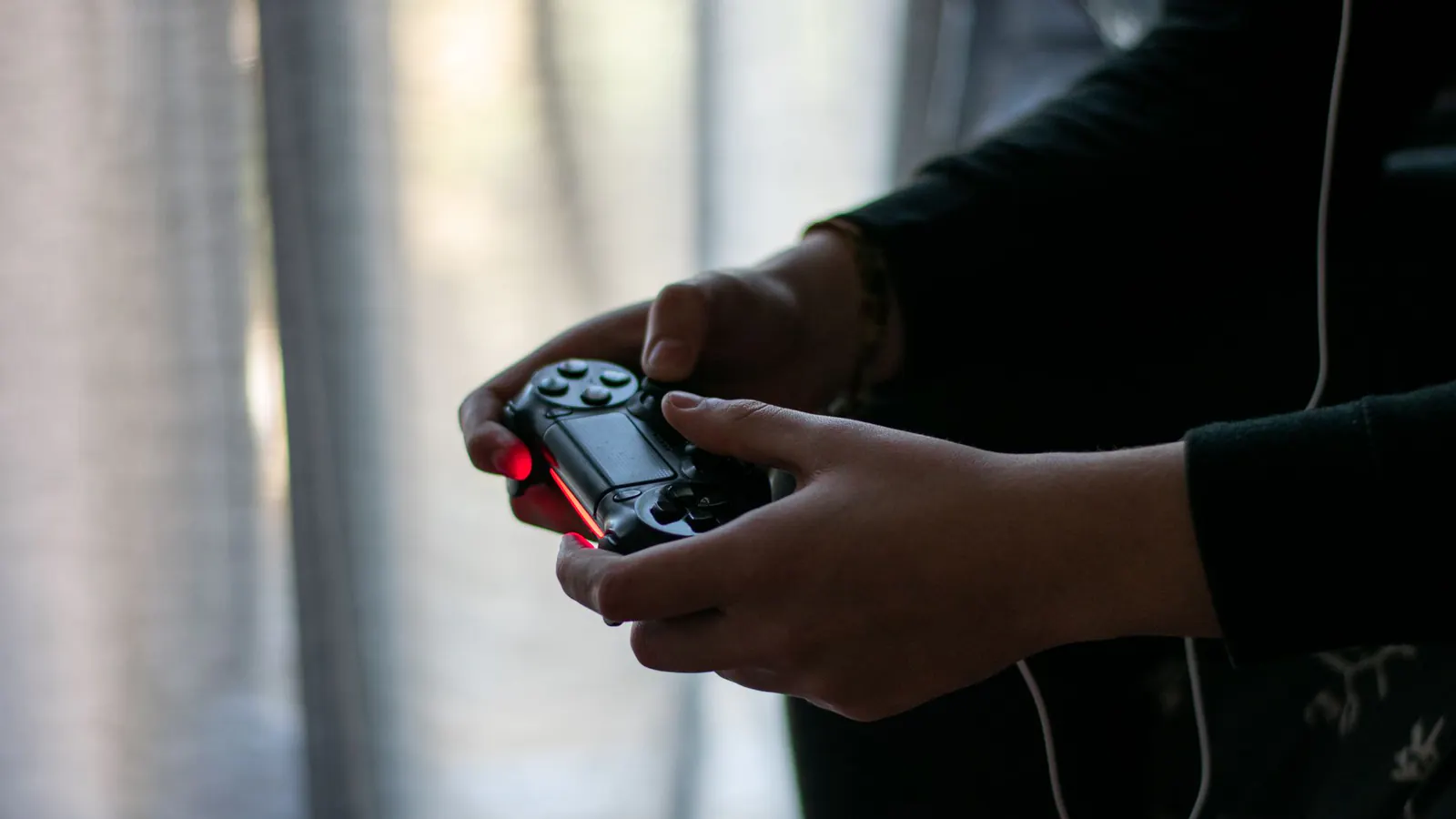 Close de mãos segurando um controle de videogame em ambiente pouco iluminado.