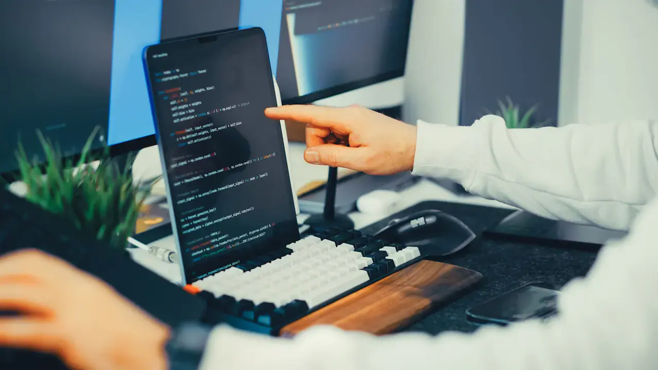 Desenvolvedor aponta para código em um notebook conectado a monitores.