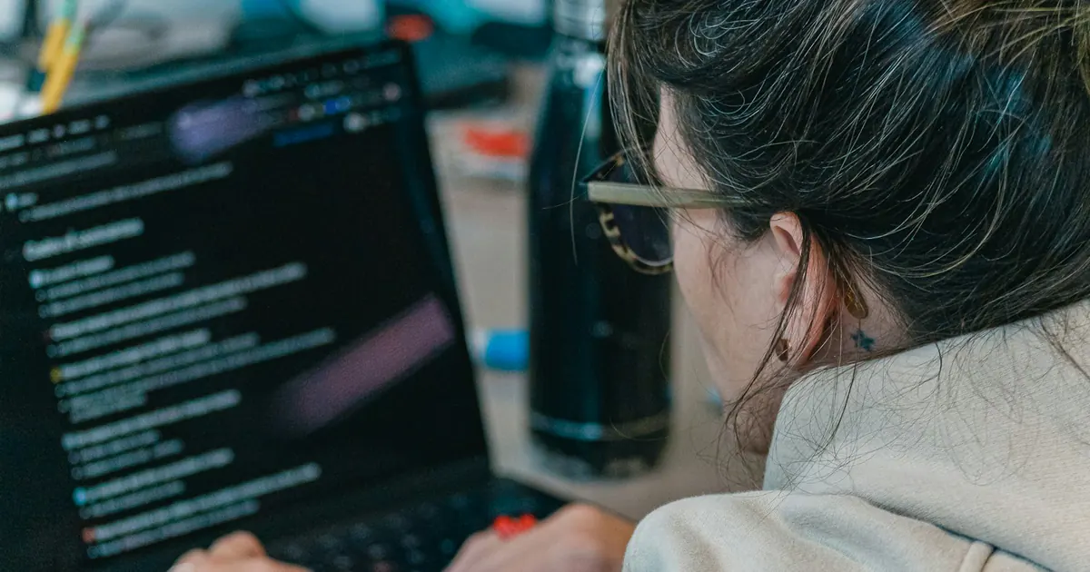 Desenvolvedora trabalha em um notebook com código na tela.