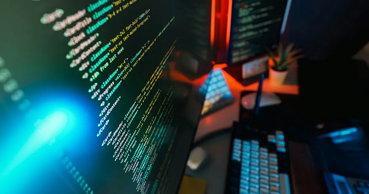 Telas de computador exibem código em um ambiente de trabalho escuro.