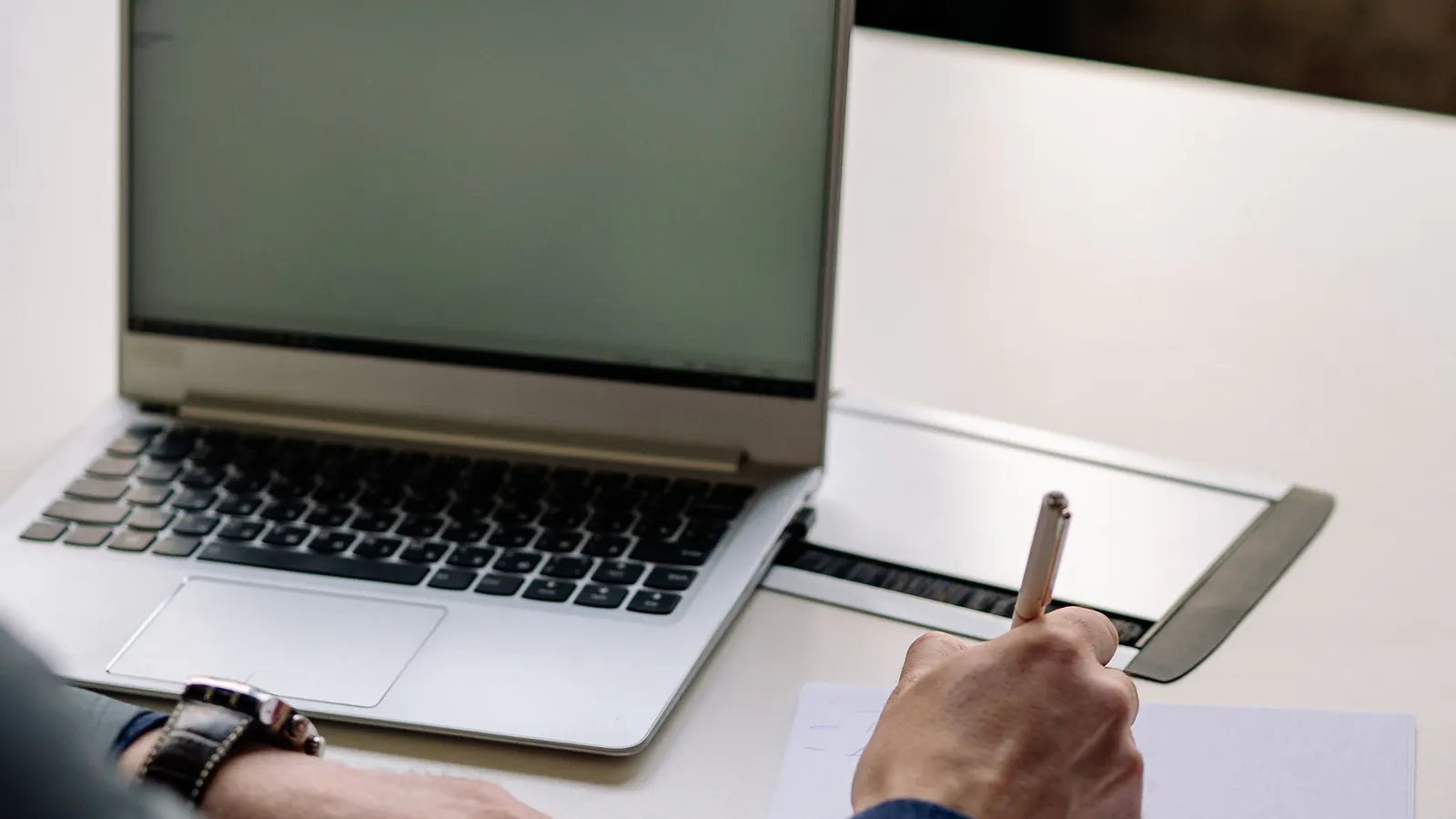 Profissional consulta documentos e anota informações ao lado de um notebook.