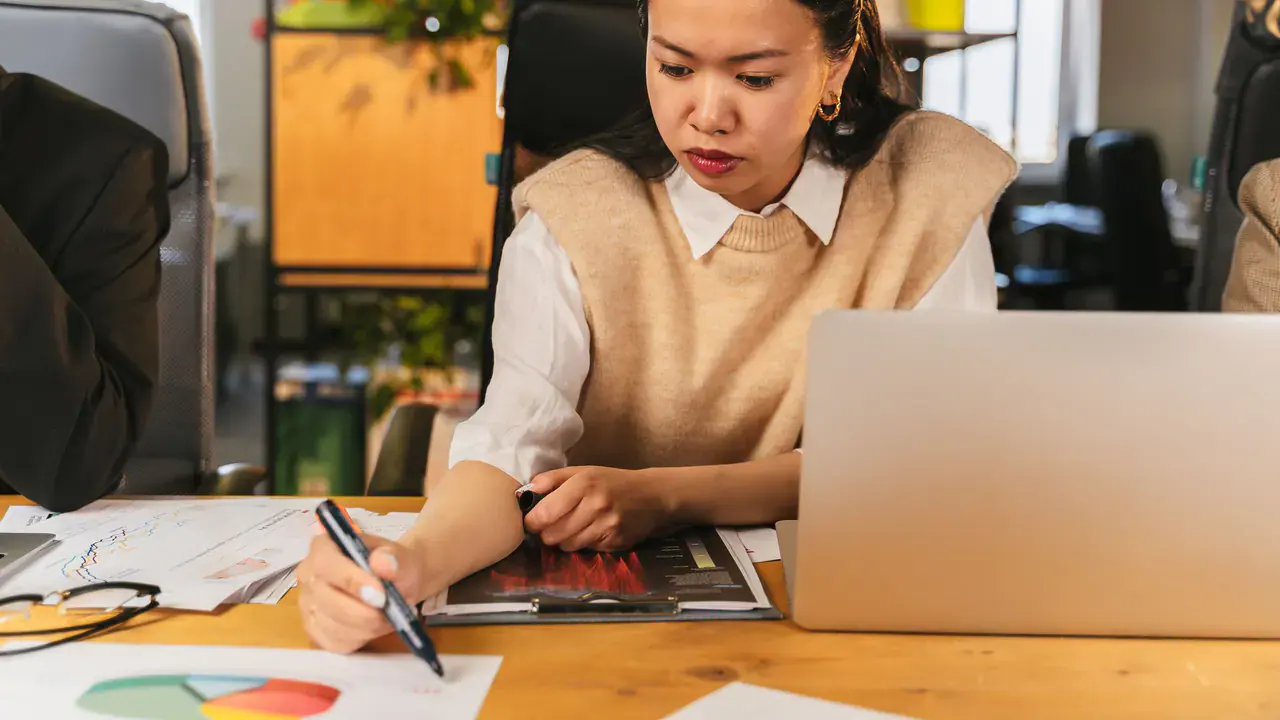 Profissional consulta anotações e notebook durante uma análise de dados.