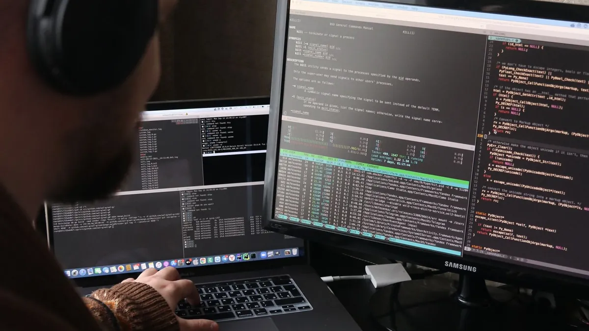 Programador trabalha com código em uma estação com computador e notebook.