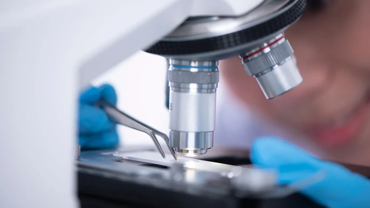 Pesquisador observa uma amostra através de um microscópio em laboratório.